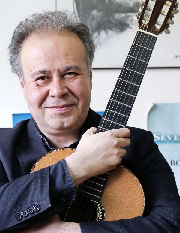 Smiling man in a dark blazer embraces a classical guitar.