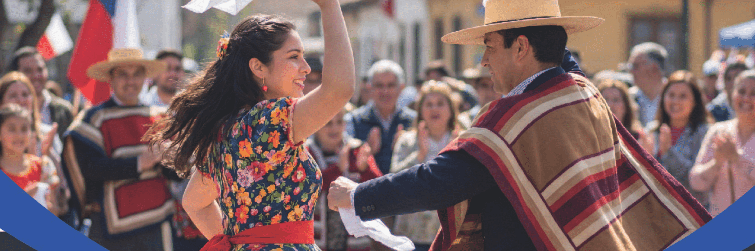Woman in a floral dress dances with a man in a poncho and hat at a lively cultural festival; crowd cheers in the background.