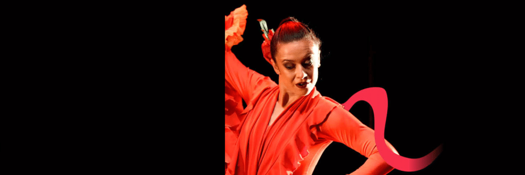 Dancer in a bright red costume performing on a dark stage with a pink flowing ribbon prop around her arm.