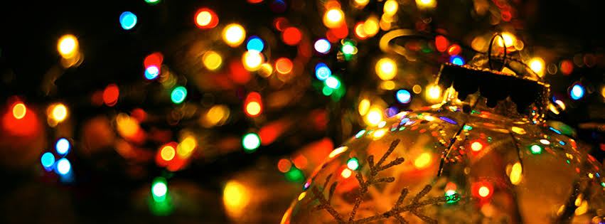 Close-up of a gold Christmas ornament with a snowflake pattern, with multicolored holiday lights in the blurred background.